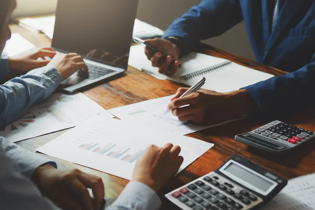 Varias manos coordinan tareas y cálculos en una reunión, un claro ejemplo de las ventajas de un sistema contable para optimizar procesos administrativos.