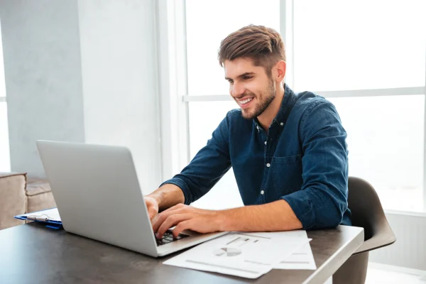 Hombre sonriendo mientras usa CONTPAQi, disfrutando de la facilidad y rapidez que ofrece el software en su computadora.
