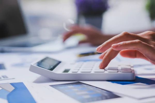Contador trabajando con CONTPAQi® Contabilidad sobre documentos contables. Manos usando CONTPAQi® Contabilidad para calcular datos financieros en una calculadora.