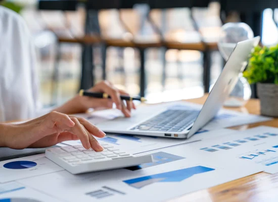 Mujer trabajando con CONTPAQi® Factura Electrónica, tecleando datos en una laptop y consultando gráficos financieros. Mujer usando CONTPAQi® Factura Electrónica en una computadora, mientras revisan documentos y usa una calculadora.