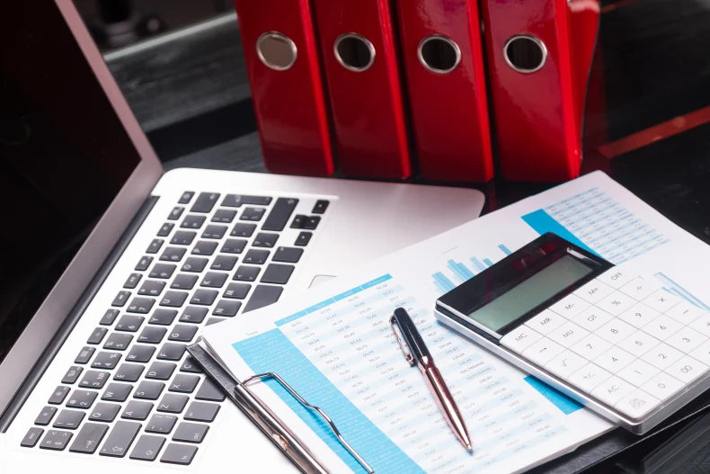 Materiales para organizar documentos contables con ayuda de un sistema administrativo, desde una laptop y calculadora de escritorio.