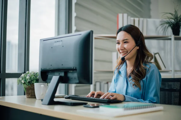 Una colaboradora atiende desde su escritorio usando audífonos con micrófono mientras observa la pantalla de su computadora, usando un sistema como CRM Zeus para gestionar la información.