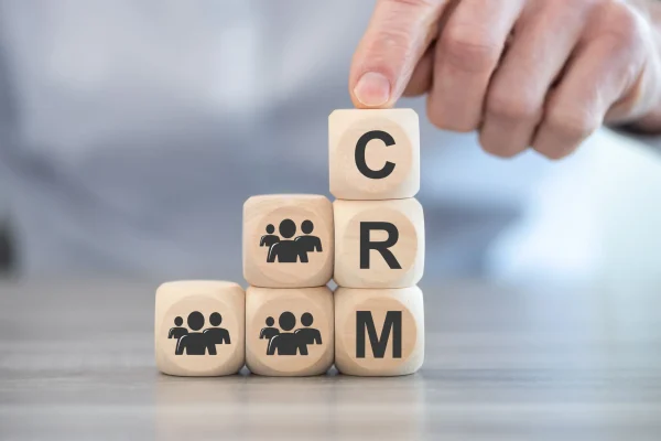 Sobre una superficie clara se alinean cubos de madera con letras que conforman la palabra CRM, centradas en la organización de relaciones con clientes.