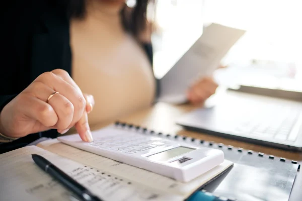 Una persona presiona revisa su calculadora y una hoja impresa en un escritorio lleno de documentos, representando el trabajo cotidiano y detallado que se reconoce cada Día del contador.