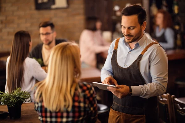 En un entorno de atención al cliente, los emprendedores también se preguntan cómo elegir el mejor software para emitir facturas electrónicas que se adapte a su operación diaria. Un mesero atiende a una clienta en un restaurante, donde también surge la pregunta cómo elegir el mejor software para emitir facturas electrónicas en el contexto de pequeños negocios.