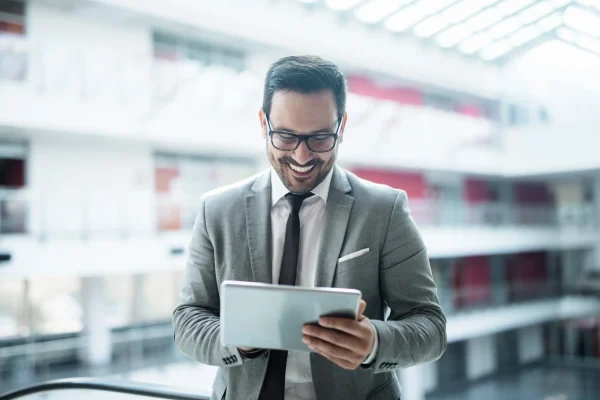 Usuario consultando contenido digital en una tablet desde un espacio iluminado, una situación común para quienes acceden a cursos desde CONTPAQi® Kursa. Un hombre con gafas revisa información en una tablet mientras sonríe, representando un momento de estudio o consulta en línea, como el de CONTPAQi® Kursa.