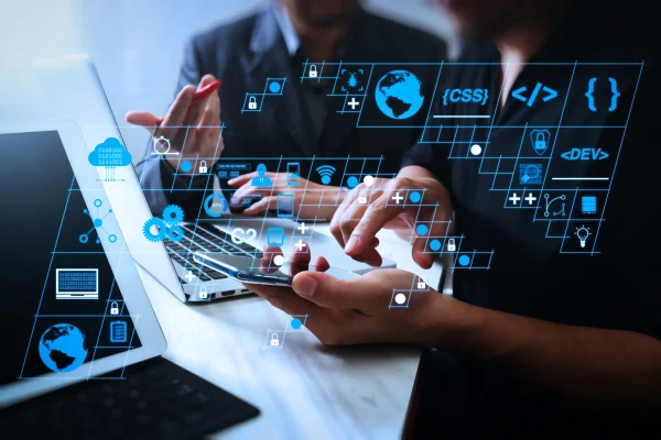 Dos personas trabajan juntas en una laptop mientras visualizan gráficos digitales que simulan interfaces de sistema de Contpaqi nube. Manos manipulando dispositivos mientras gráficos flotantes con íconos de software que son posible gracias al uso de herramientas como Contpaqi nube en un ambiente colaborativo.