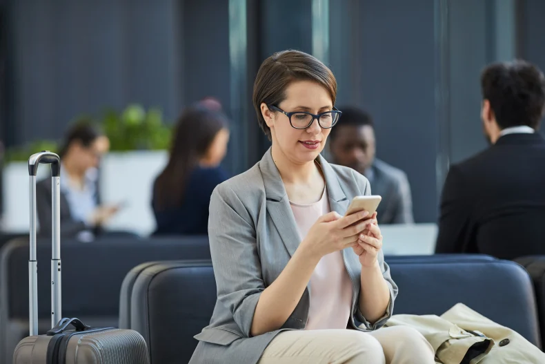 Una mujer revisa su celular en un entorno laboral, posiblemente consultando información relacionada con la prima vacacional en México.