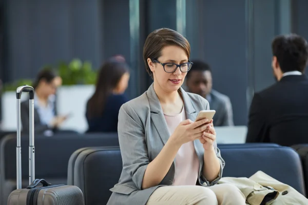 Una mujer revisa su celular en un entorno laboral, posiblemente consultando información relacionada con la prima vacacional en México.