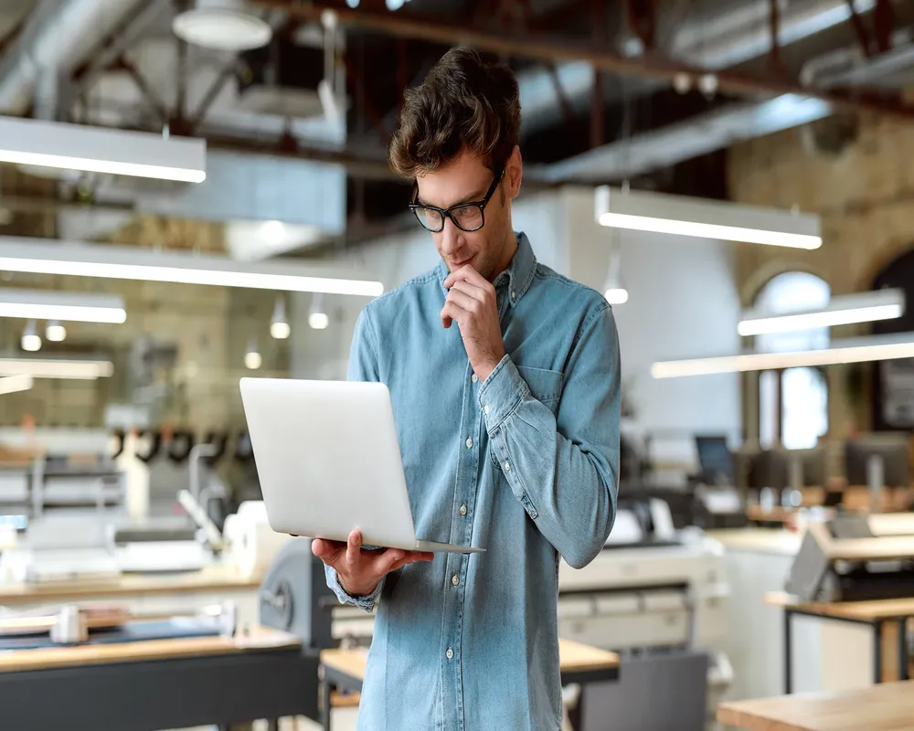 Profesional revisando información relacionada con Regímenes Fiscales en su computadora portátil dentro de un espacio de trabajo industrial.