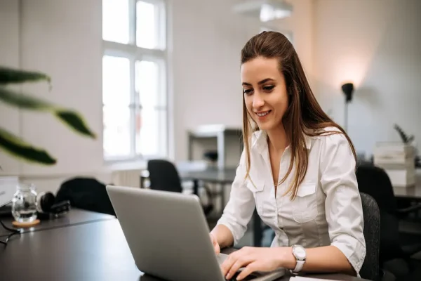 Uso de software administrativo para gestionar tareas desde una laptop en un entorno de oficina, con una mujer concentrada en su trabajo.