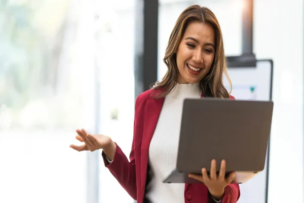 Interacción con software administrativo desde una laptop, con una mujer sonriente que sostiene el equipo mientras participa en lo que parece ser una reunión o presentación virtual.
