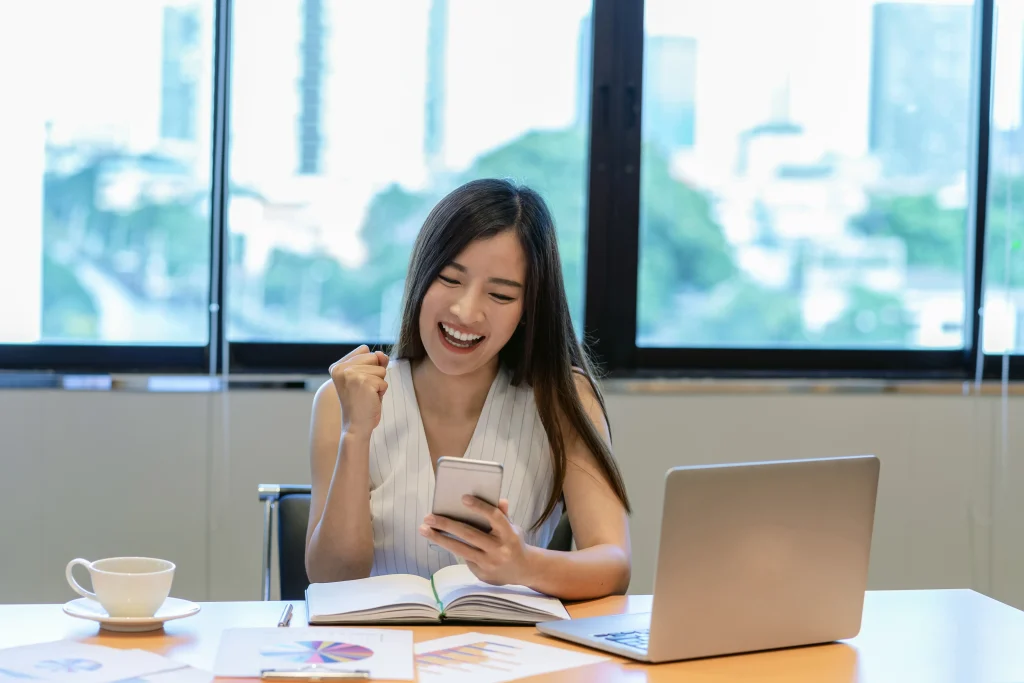 Una joven consulta su teléfono mientras trabaja en laptop, representando la practicidad de CONTPAQi® Contabilidad VS CONTPAQi® Contabiliza.