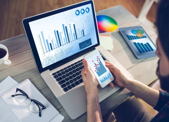 La combinación de computadora y smartphone refleja la practicidad en procesos de CONTPAQi® Factura electrónica. Una laptop con gráficas y un celular en uso representan la gestión de datos vinculada a CONTPAQi® Factura electrónica.