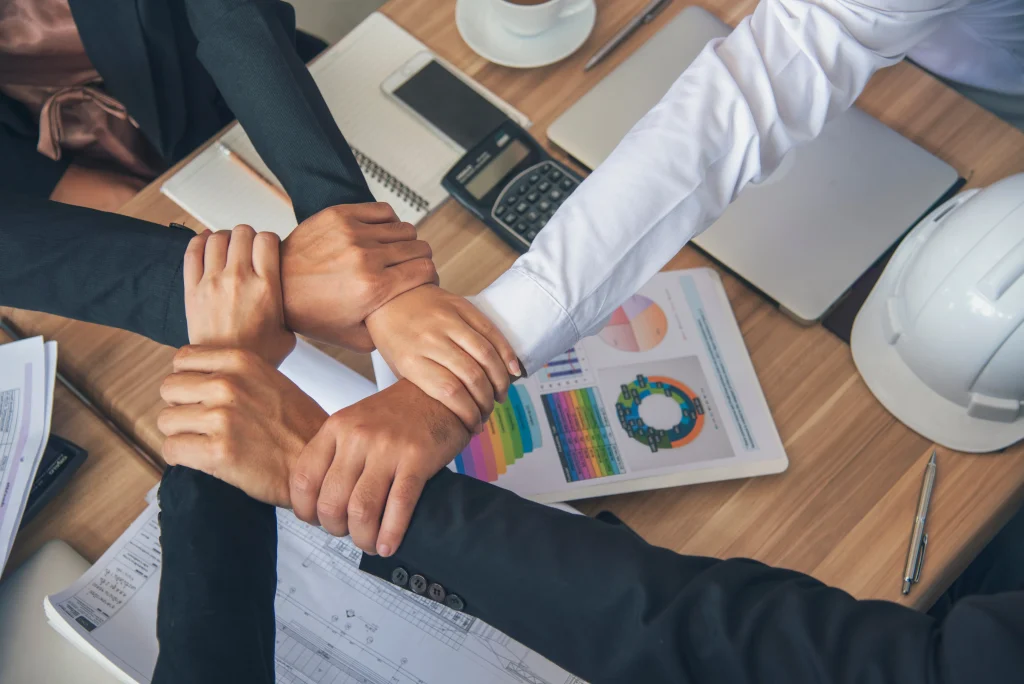 Varios profesionales unen sus manos sobre documentos con gráficas, simbolizando la confianza y cooperación necesarias para fortalecer las soluciones de gestión de riesgos.