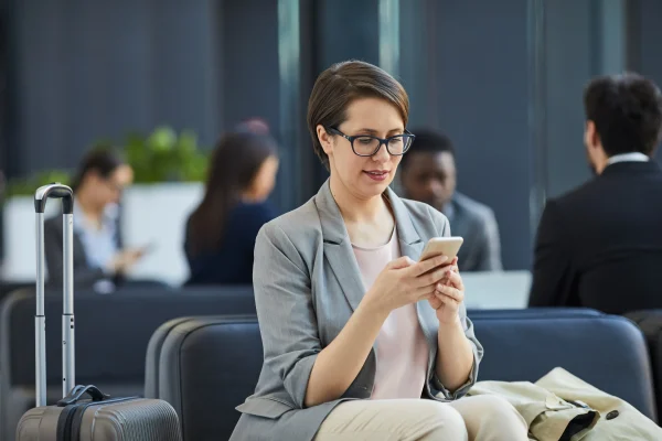 Una mujer consulta su teléfono con una maleta a un lado, registrando sus movimientos de viaje con apoyo de Contpaqi viáticos.