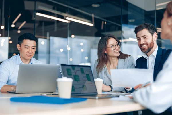 Personas colaboran alrededor de una mesa con papeles y pantallas, apoyándose en Contpaqi personia para coordinar tareas. Un equipo conversa mientras revisa laptops y documentos, mostrando cómo Contpaqi personia se integra en su organización diaria.