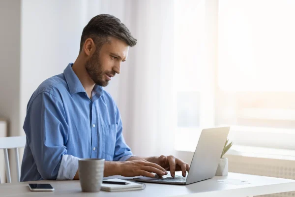Un profesional escribe en su computadora junto a la ventana, gestionando datos con Contpaqi personia. Un hombre trabaja concentrado en su laptop, utilizando Contpaqi personia para ordenar su información.