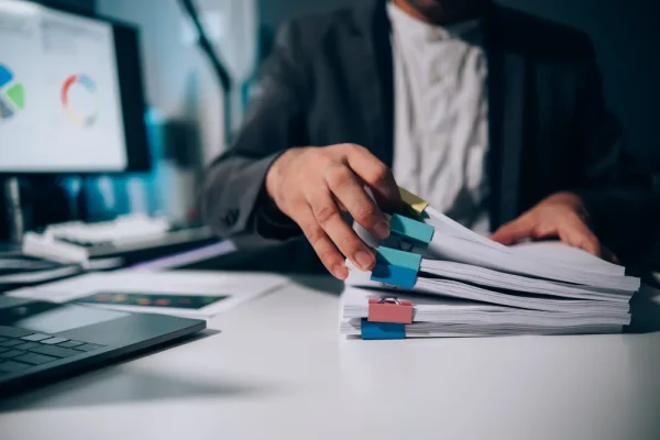 Vista general de una persona revisando expedientes de empleados que tiene sobre su escritorio.