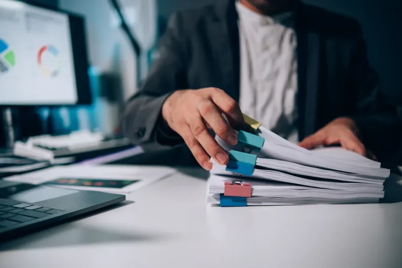 Vista general de una persona revisando expedientes de empleados que tiene sobre su escritorio.