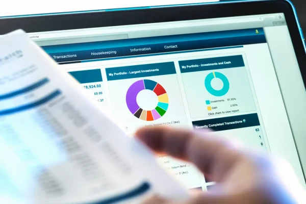 El software de análisis financiero de una empresa. Enfoque en la laptop en donde se puede alcanzar a ver los resultados del software de análisis financiero, mientras una persona sostiene una hojas.