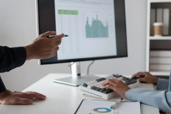 Una escena comparativa donde se vea una computadora con un software contable moderno frente a hojas de Excel puestas en el escritorio.