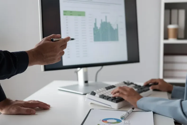 Una escena comparativa donde se vea una computadora con un software contable moderno frente a hojas de Excel puestas en el escritorio.
