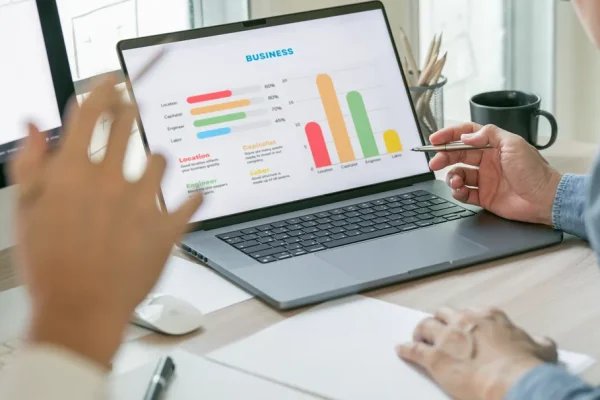 Gráficos financieros digitales que aparecen en una laptop, mientras unas personas lo están analizando.