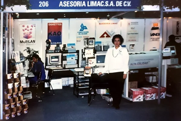 Fotografía antigua de un evento de exposición de la empresa. Vista general de un stand de la empresa LIMAC en un lugar de expositores y una mujer en el frente posando.