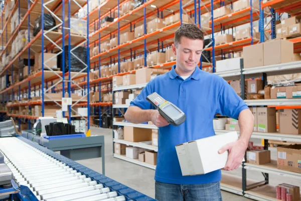 Control dentro de la venta con el sistema CONTPAQi® Comercial premium. Vista general de un hombre en un almacén en donde se puede observar como realizar el scanner de una caja para mayor control, gracias al sistema de CONTPAQi® Comercial premium.